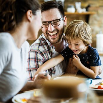A dad laughs as his child grabs a fork at the dinner table.
